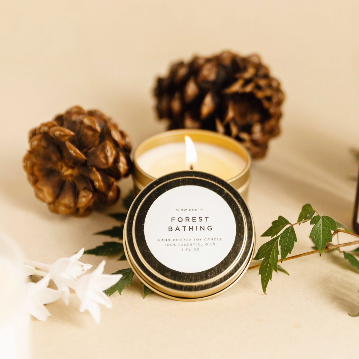 Scented candle in gold metal tin with lit wick and circular lid label