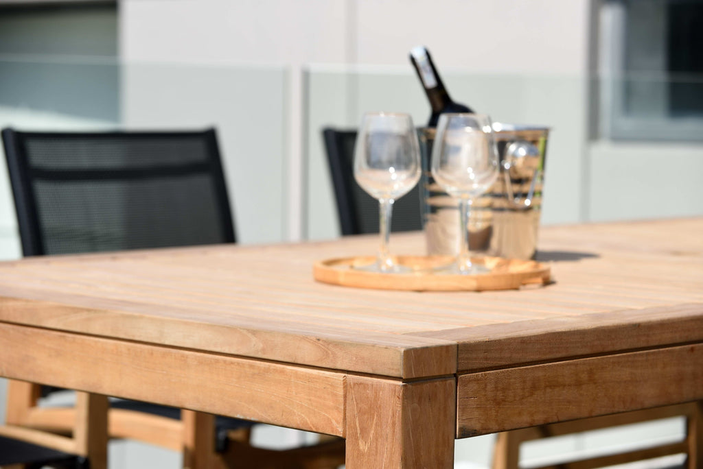Close-up of teak table top with wine glasses and bottles set for dining