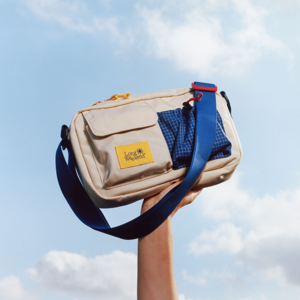 Cream shoulder bag with blue crossbody strap and flap front pocket.