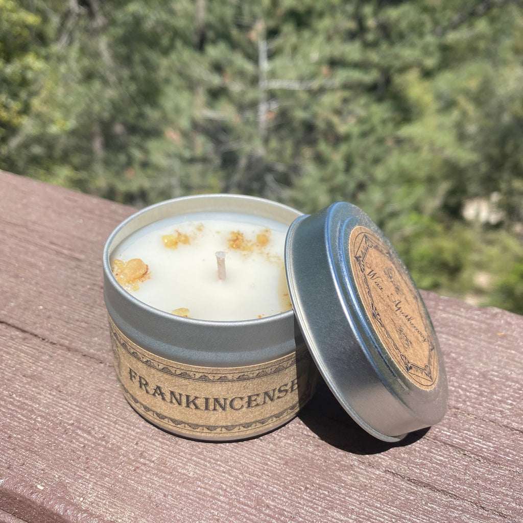 Open travel candle tin with white candle and blue-tinted silver lid, tan label band