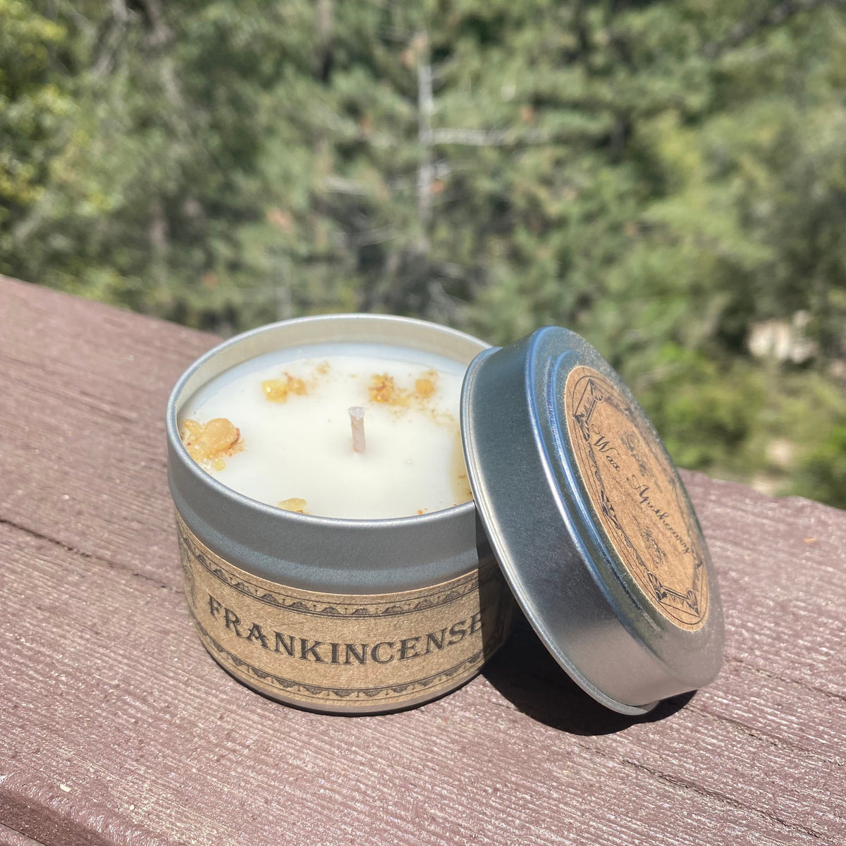 Open travel candle tin with white candle and blue-tinted silver lid, tan label band