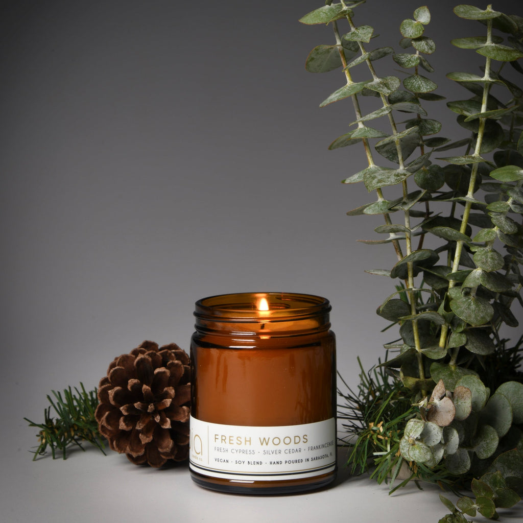 Amber glass candle jar with lit wick and Fresh Woods label, dark brown wax