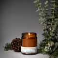 Amber glass candle jar with lit wick and Fresh Woods label, dark brown wax