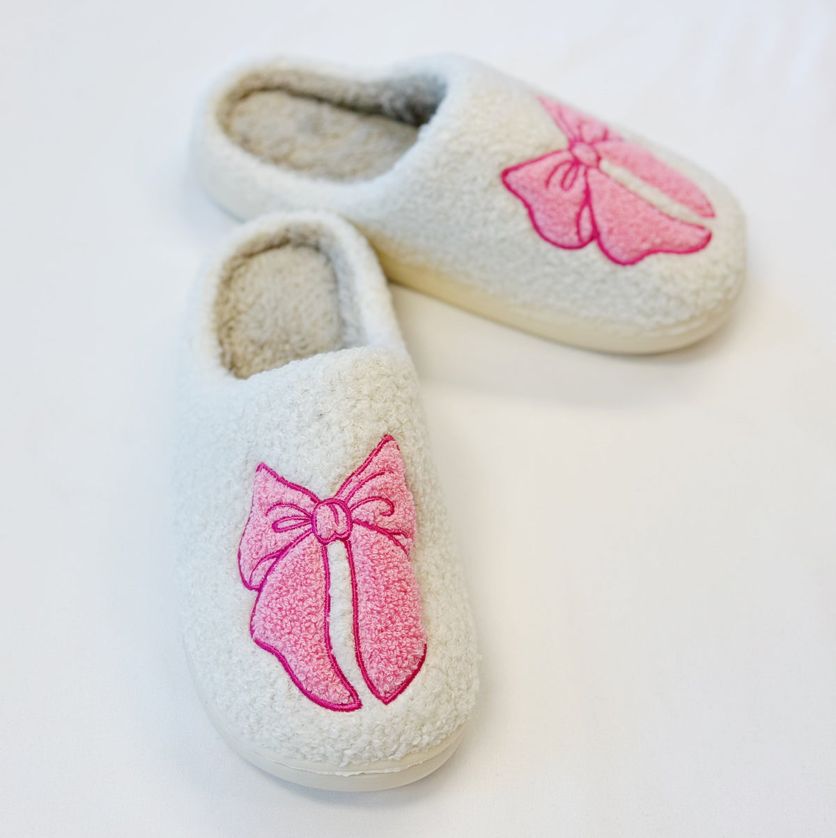 Cream cozy slippers with pink bow appliques and plush closed-toe uppers