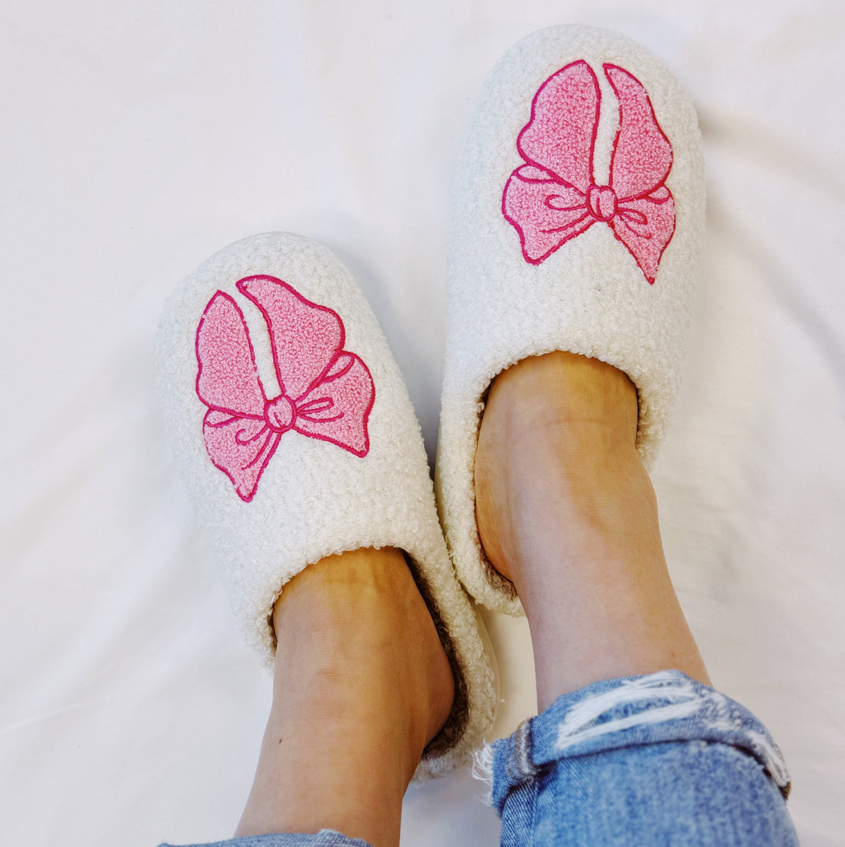 Pair of cream slip-on slippers with pink bow patches and soft interior lining