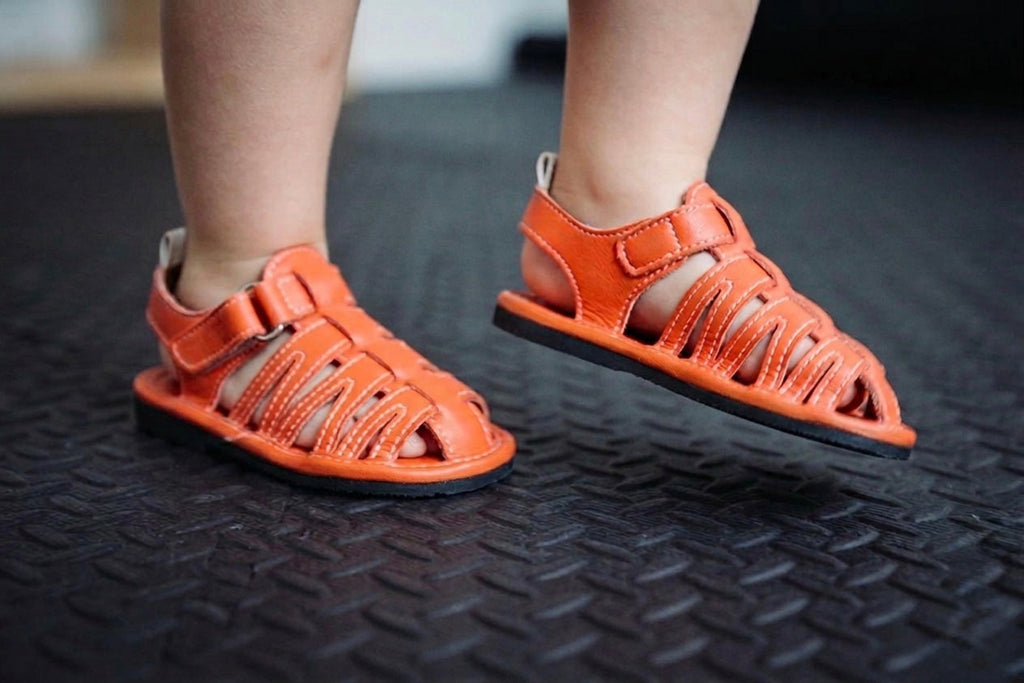 Pair of orange kids sandals with velcro strap and open-toe design