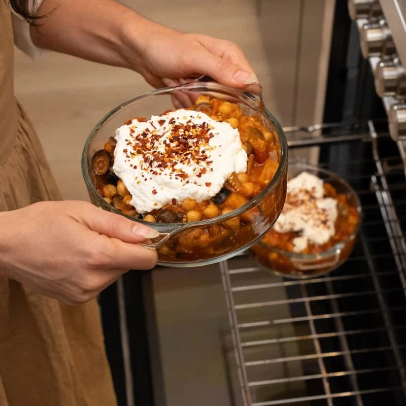 Glass casserole dish with lid, filled with baked beans and topping, held by hands
