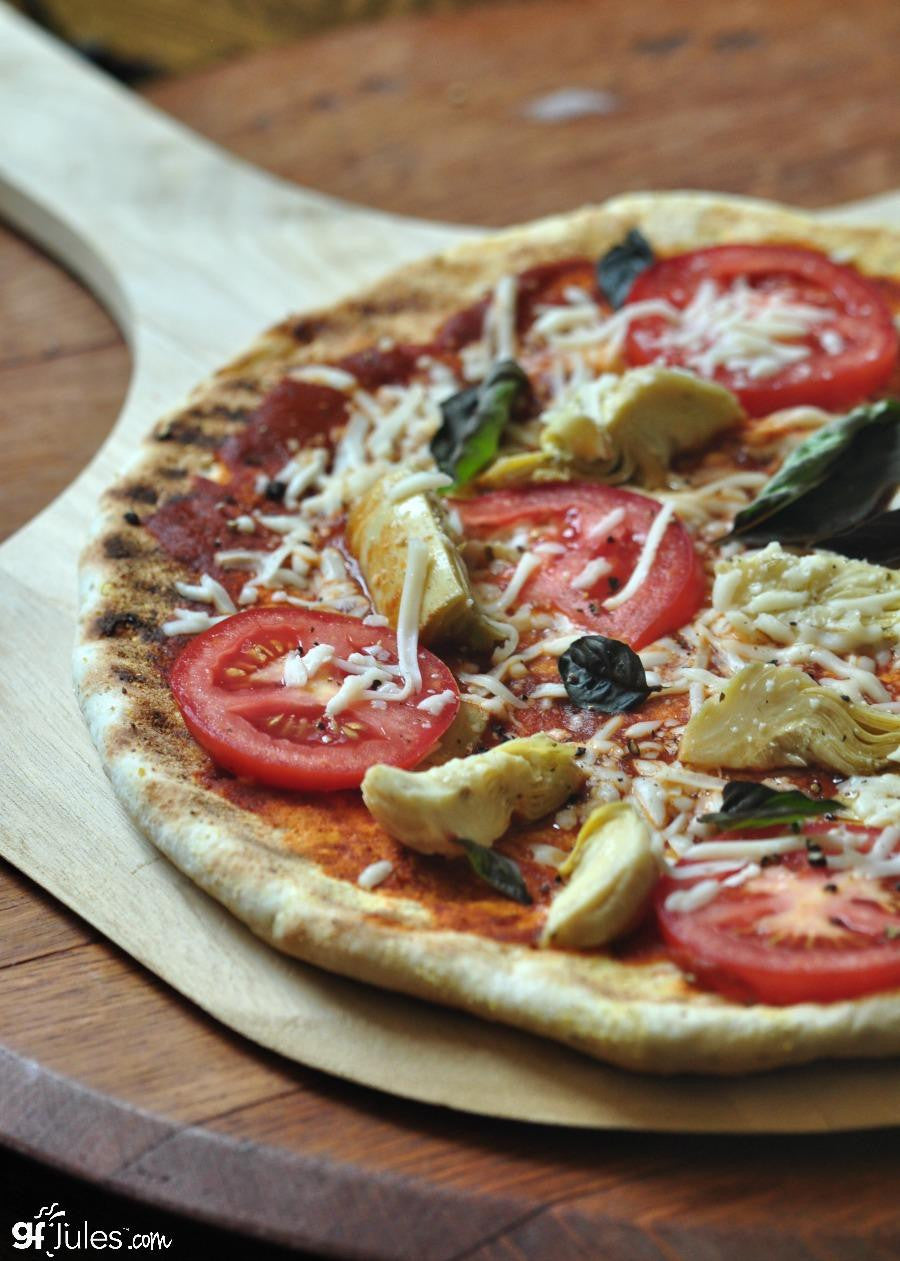 Gluten-free pizza on parchment with sliced tomatoes, olives, and herbs