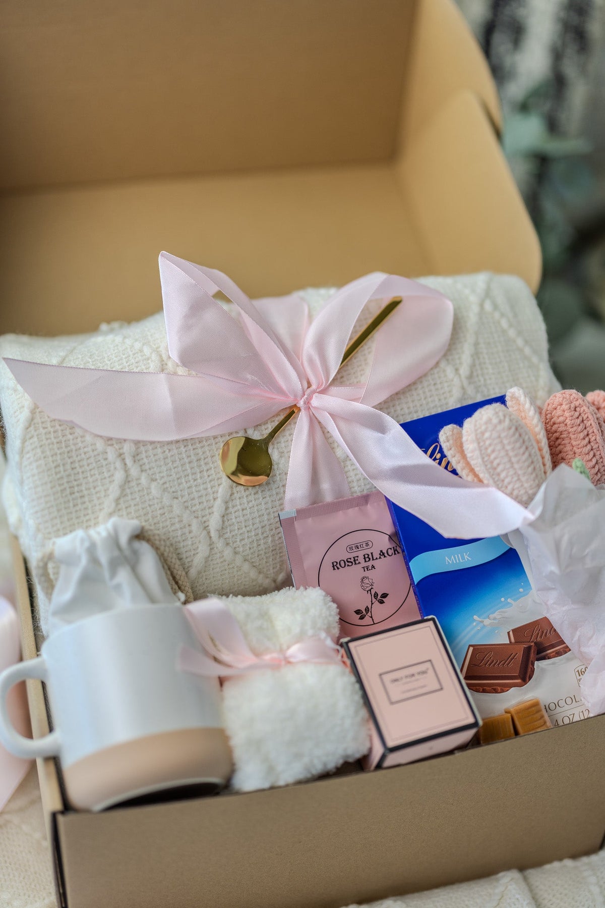 Pink gift care package in open box with ribbon, candles, and bath items