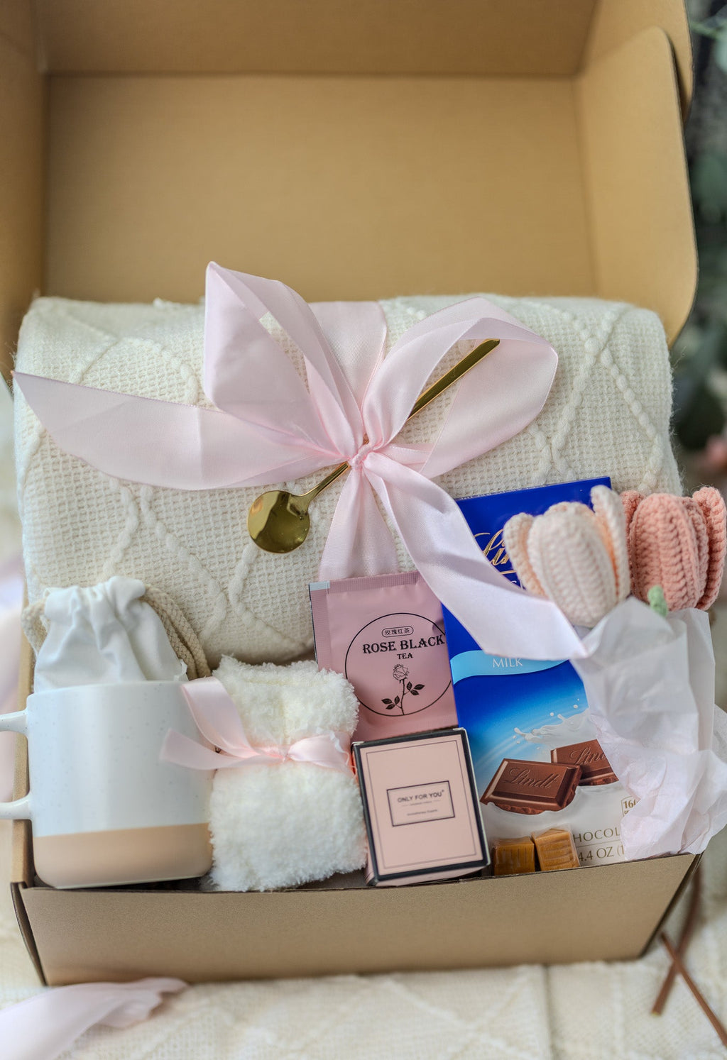 Pink gift care package in open box with ribbon bow, candle, and soap set