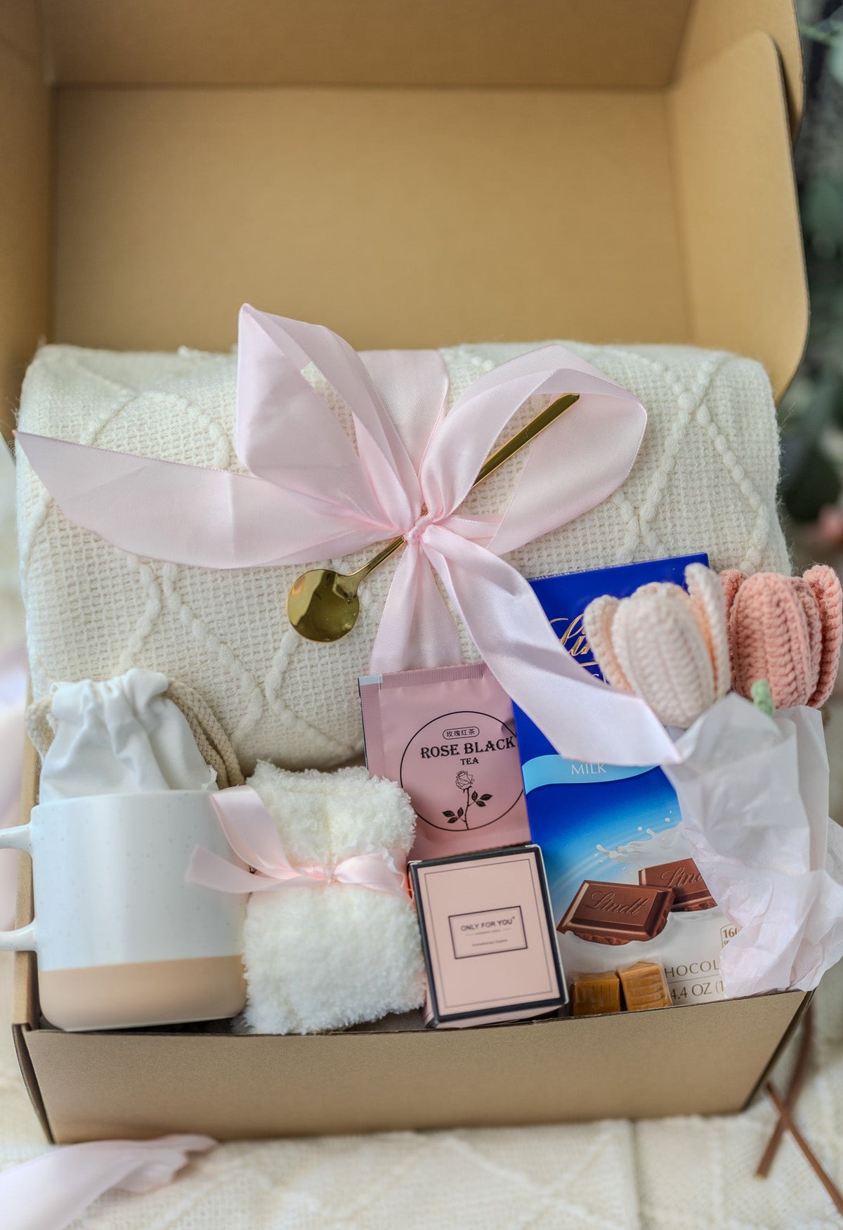 Pink gift care package in open box with ribbon bow, candle, and soap set