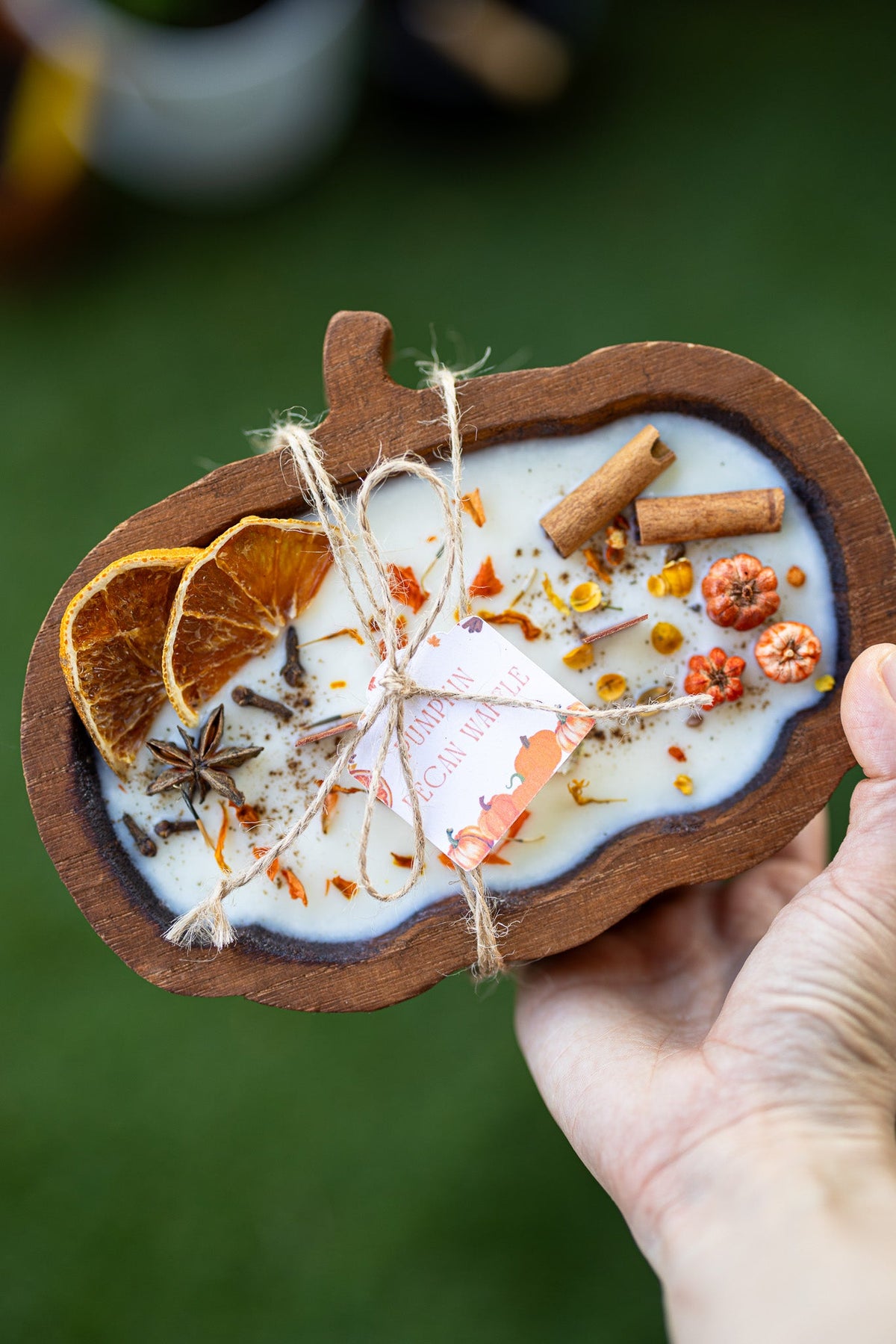 Hand holding wooden pumpkin-shaped dough bowl candle with white wax and cinnamon sticks