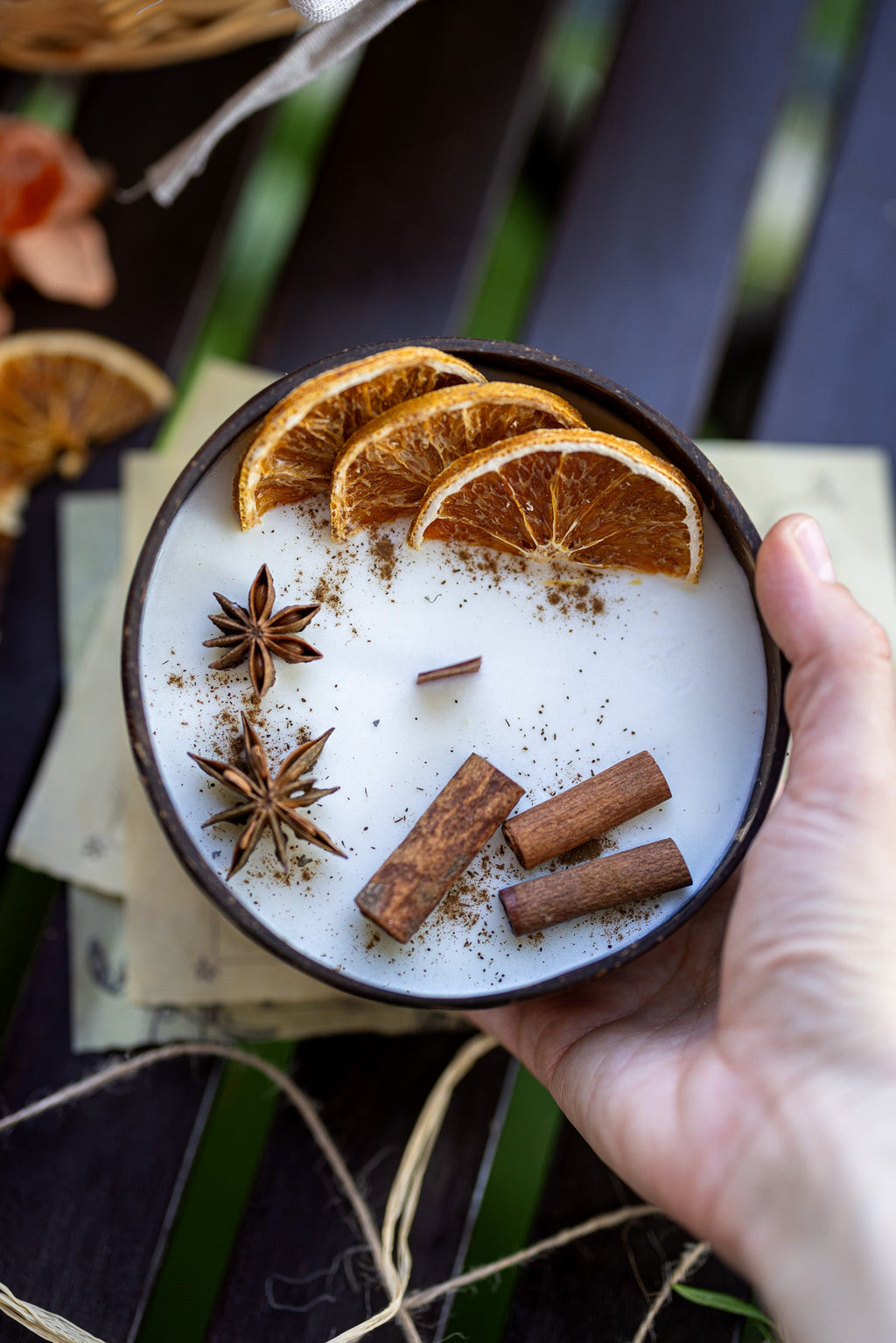Hand holding scented candle bowl with white wax, orange slices, cinnamon sticks, star anise