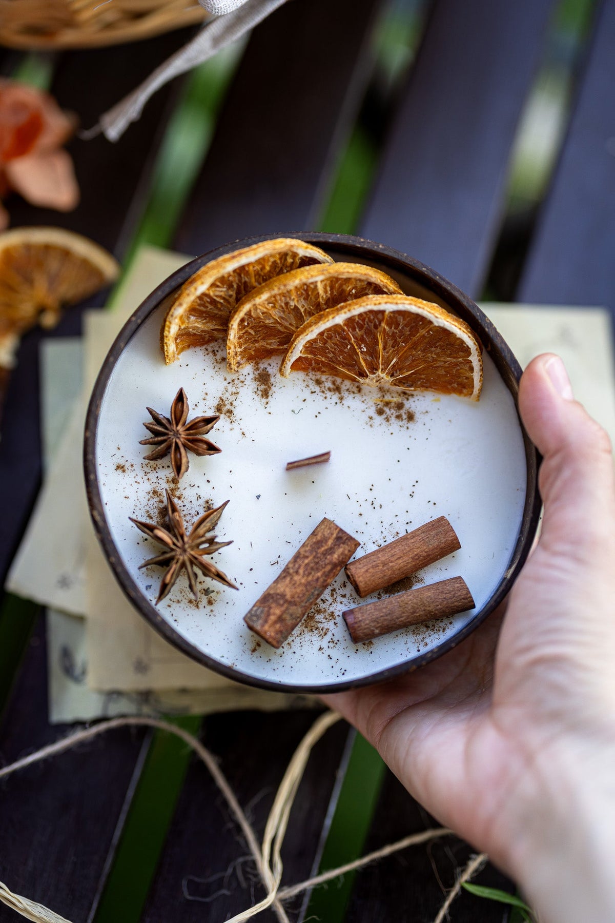 Hand holding scented candle bowl with white wax, orange slices, cinnamon sticks, star anise