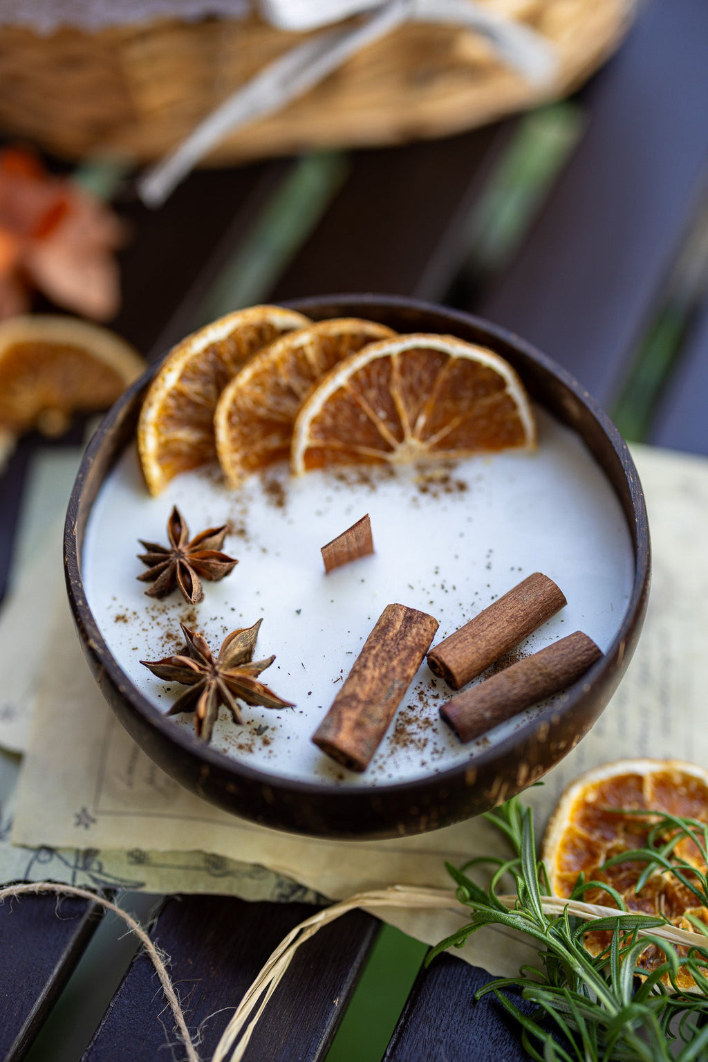 Scented candle in dark bowl with white wax, orange slices, cinnamon sticks, star anise
