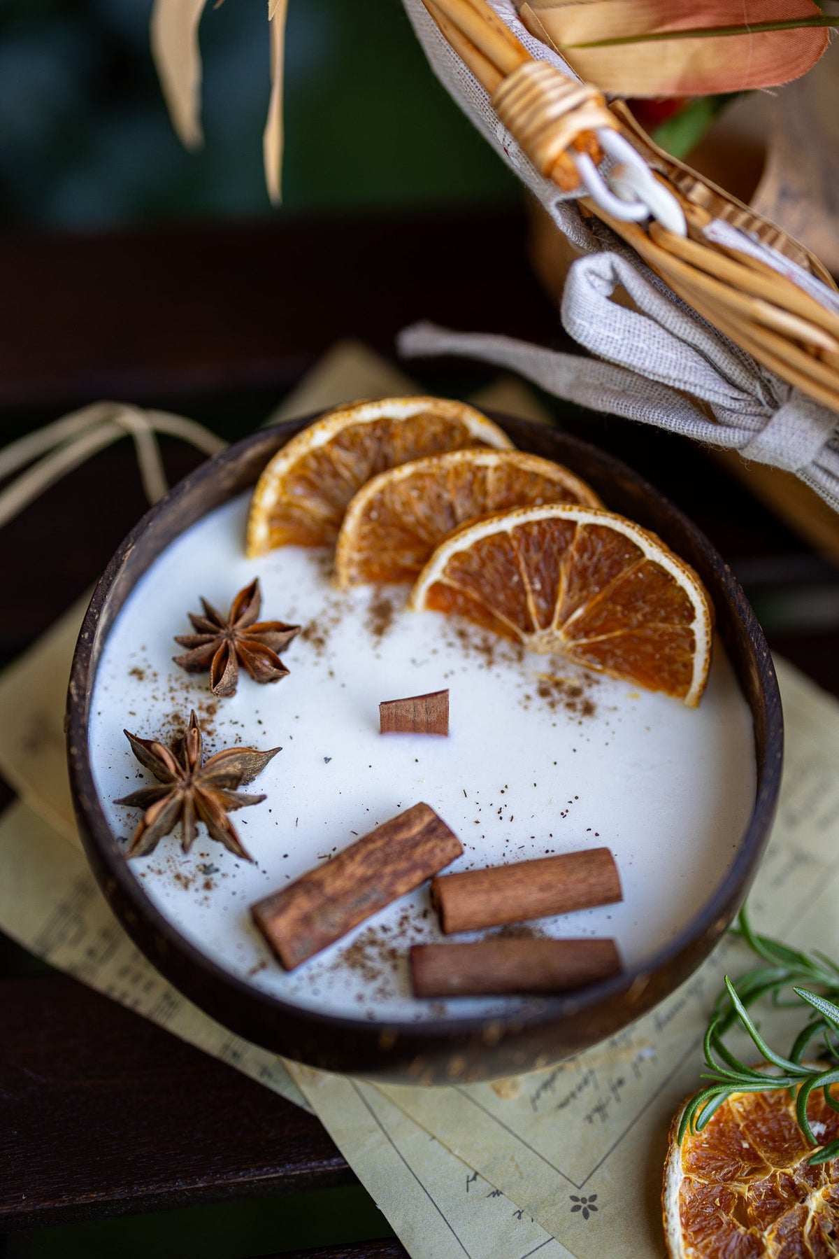Scented candle in dark bowl with white wax, orange slices, cinnamon sticks, star anise