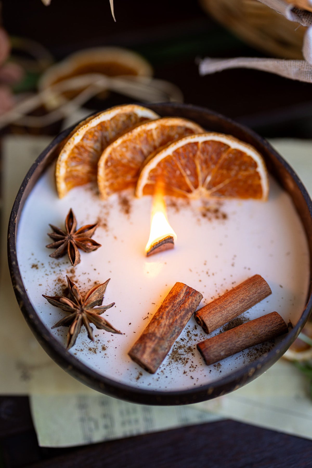 Scented candle in dark bowl: white wax with orange slices, cinnamon sticks, star anise