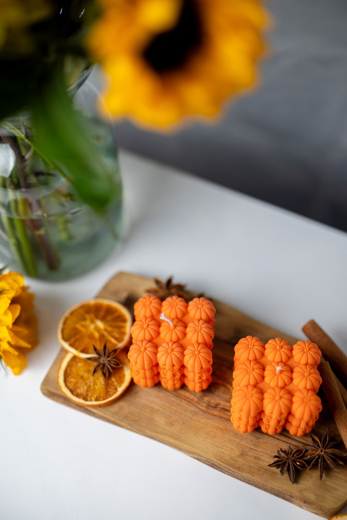 Orange pumpkin face bubble soy candles in a row on wooden tray with cinnamon and clove accents