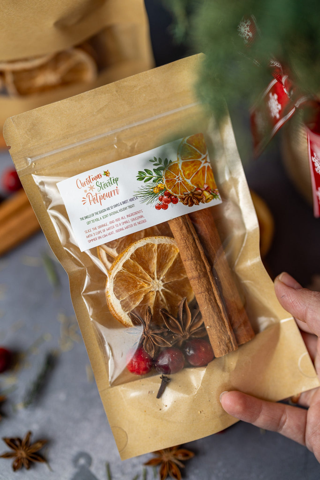 Stovetop potpourri pouch held in hand, with dried orange, cinnamon sticks, and spices
