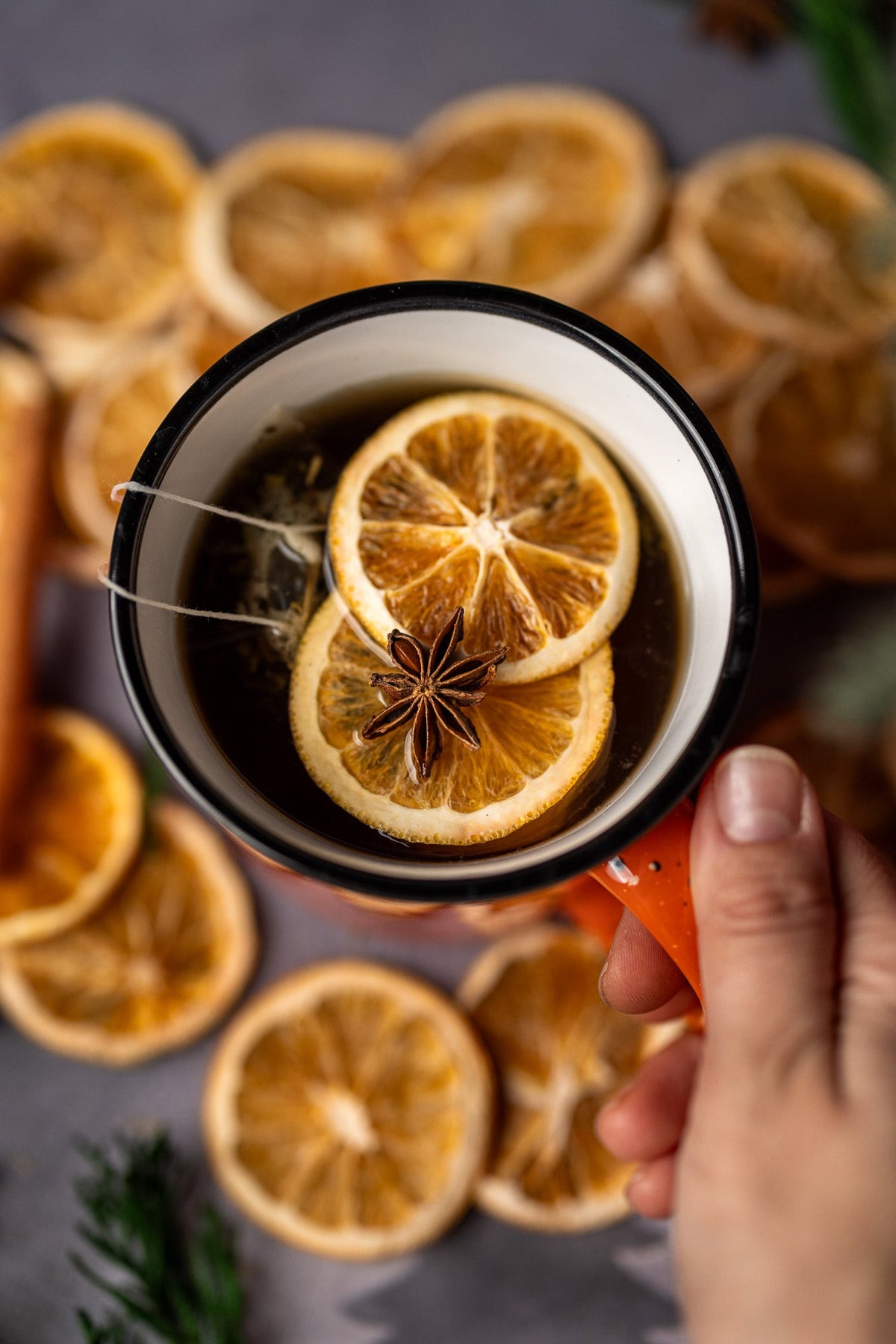 Hand holding mug of spiced stovetop potpourri with orange slice and star anise