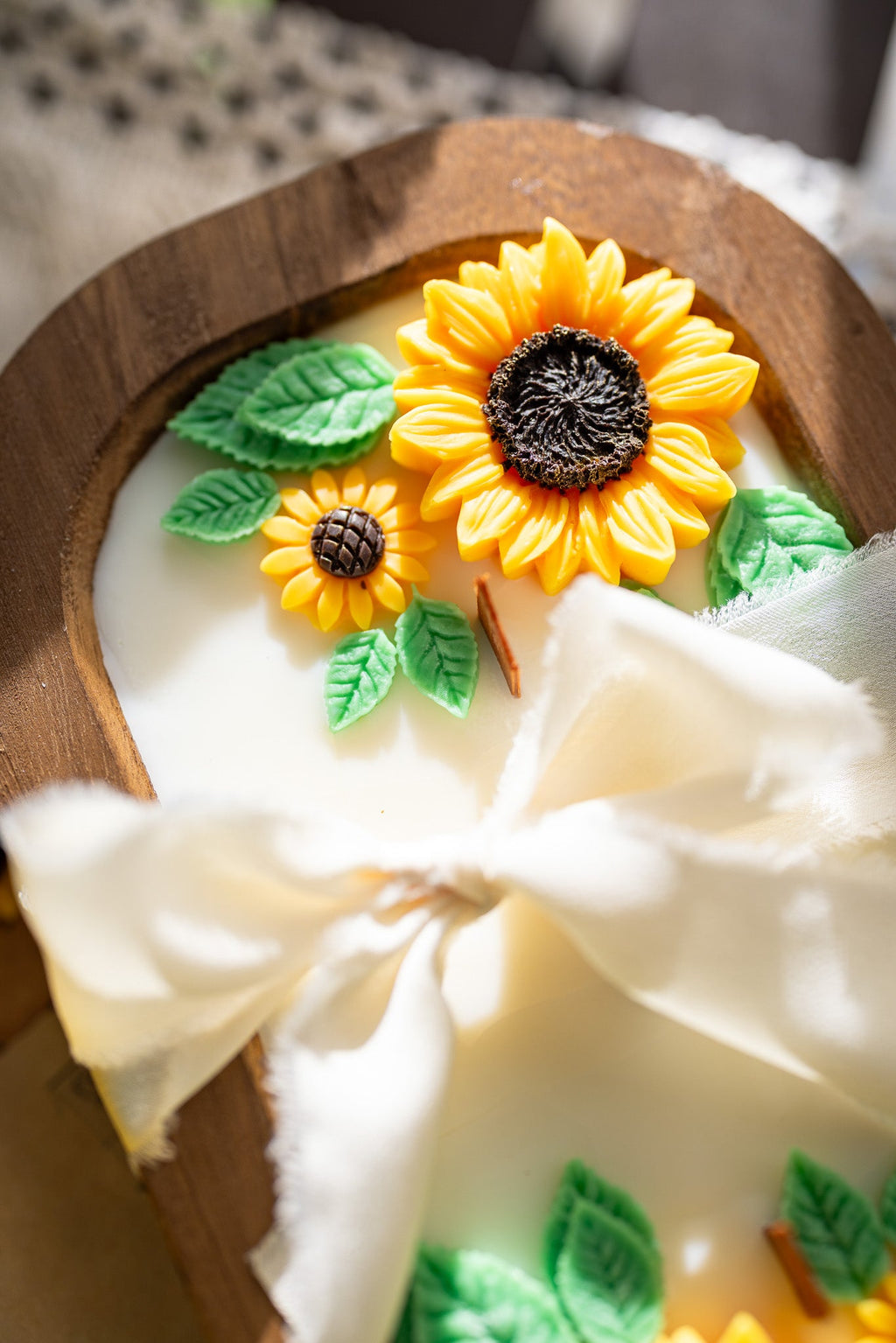 Close-up wooden sunflower soy wax candle with yellow sunflower details, green leaves, white ribbon bow