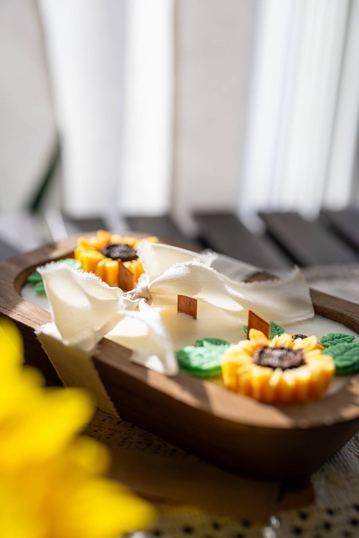 Wooden oval sunflower soy wax candle with white ribbon bow and yellow sunflower wax flowers, partial view