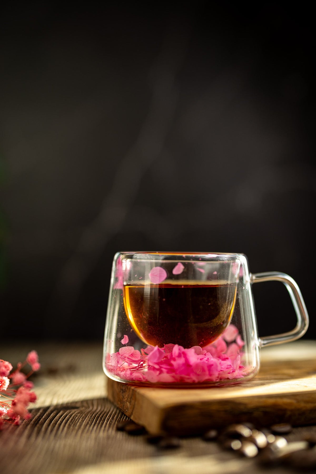 Floral glass mug with pink dried flower petals and clear handle, filled with dark tea