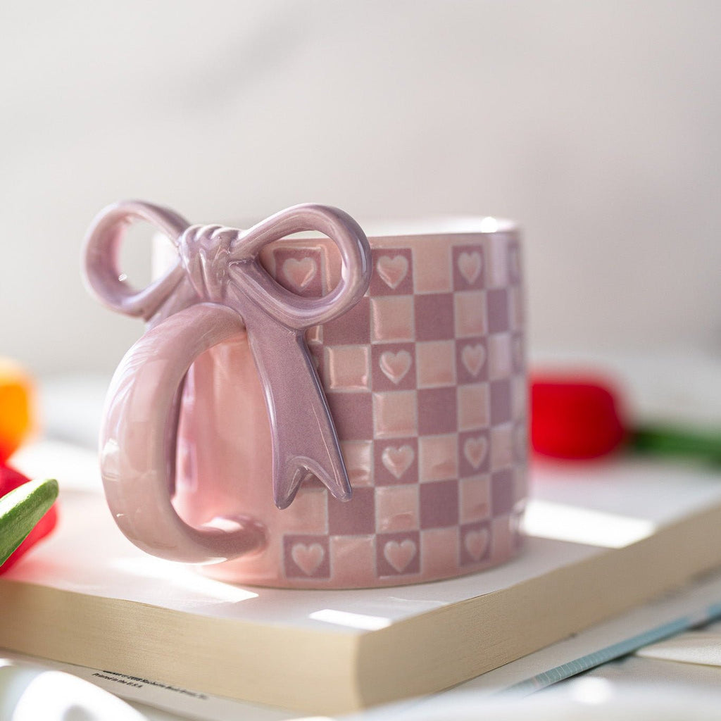 Ceramic mug in light purple with checkered heart pattern and bow ribbon handle detail
