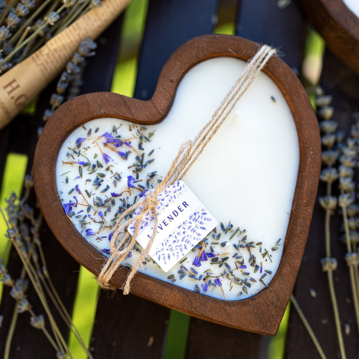 Heart-shaped wooden bowl candle with white wax and scattered lavender flowers, tied wick.