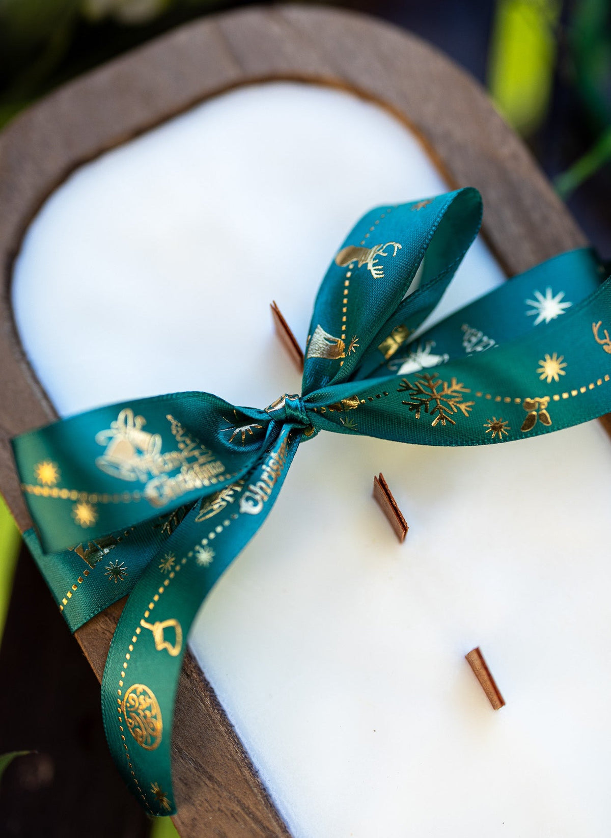 Wood dough bowl candle with teal ribbon bow across white wax oval, wick sticks visible