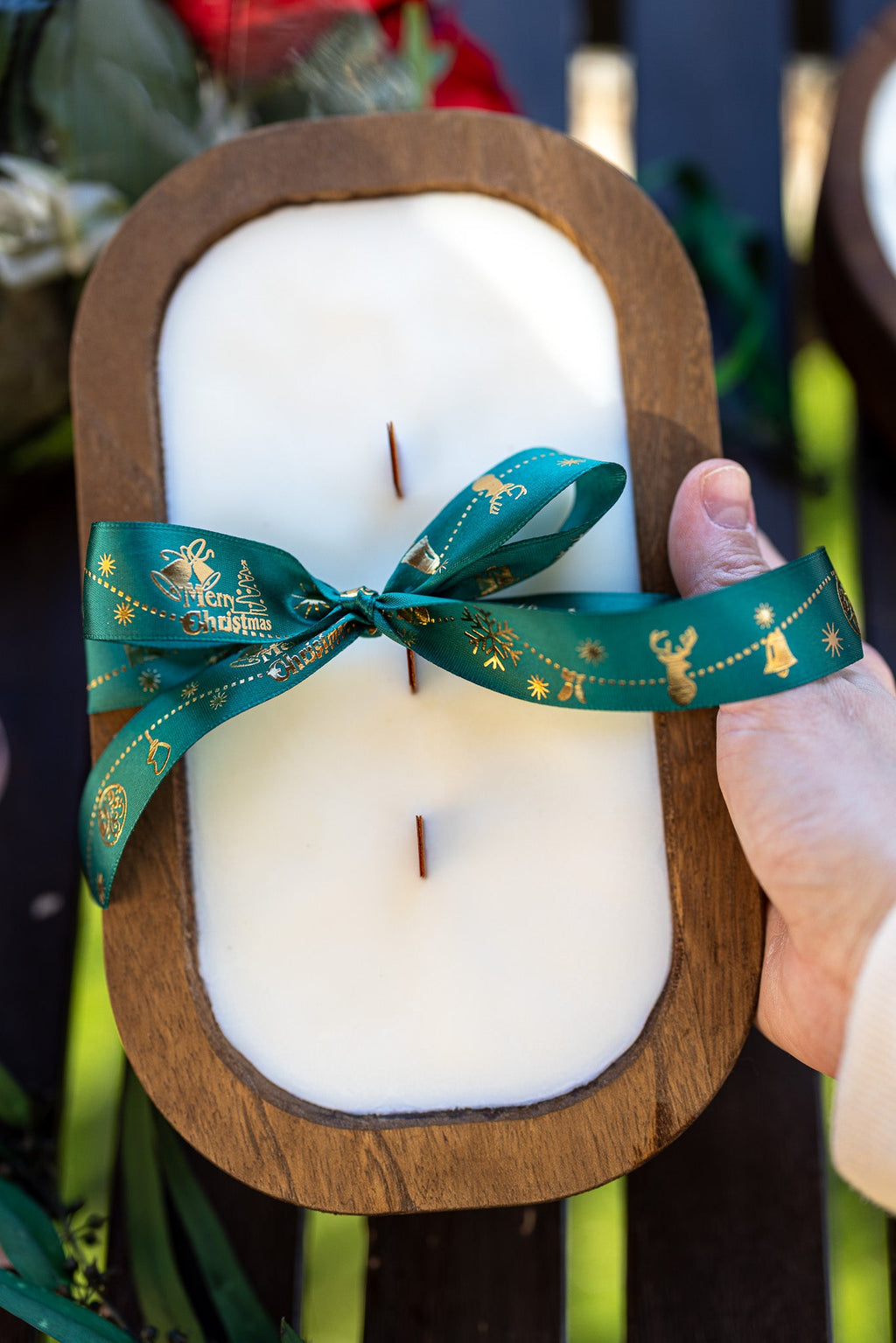 Wood dough bowl candle with white wax and teal ribbon bow, wick sticks, held by hand