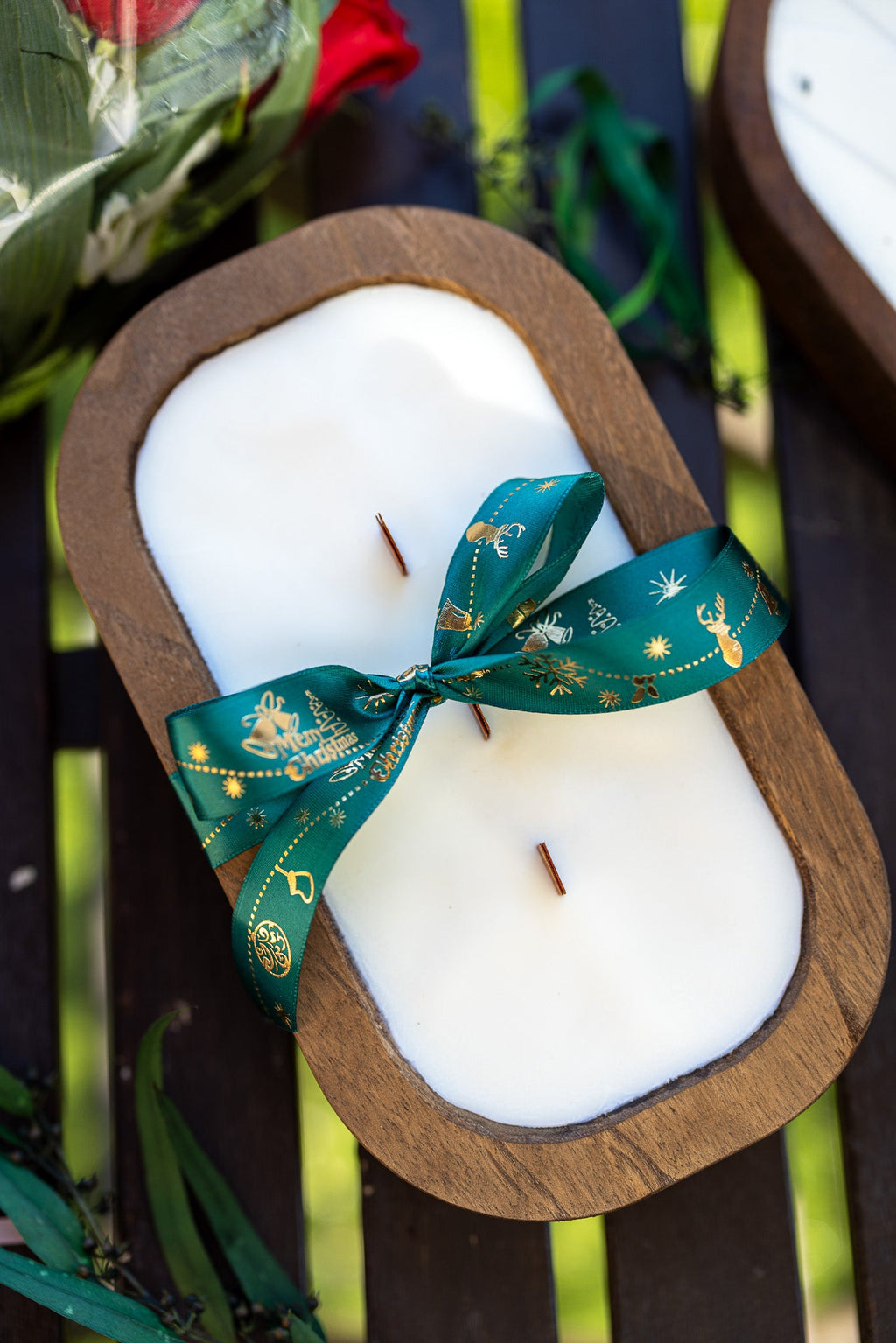 Wood dough bowl candle with white wax and teal holiday ribbon bow in brown wooden bowl