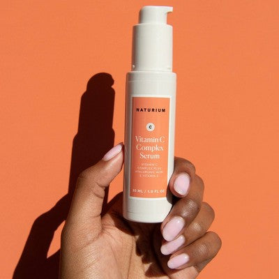 Naturium Vitamin C Complex Serum bottle held by hand with white pump and coral label