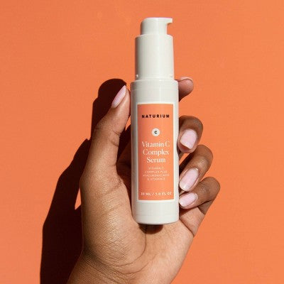 Naturium Vitamin C Complex Serum bottle with white pump, coral label, held upright