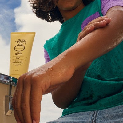 Caregiver applying sunscreen to a child’s arm with a yellow Kids SPF 50 tube