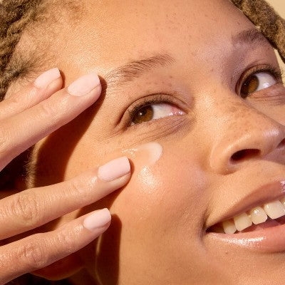 Eye balm being applied around eye with fingertips, visible translucent cream
