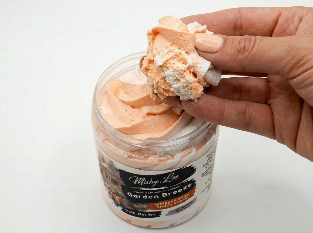 Hand holding a scoop of peach whipped soap and shave cream from clear jar