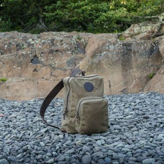 Light beige backpack on rocky ground with front zip pocket and shoulder strap