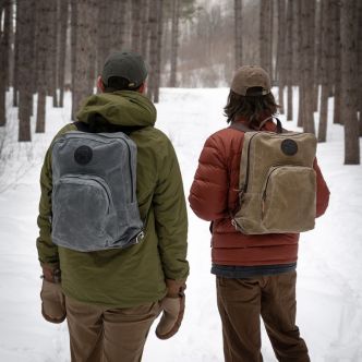 Olive green backpack worn by two people walking in snowy forest