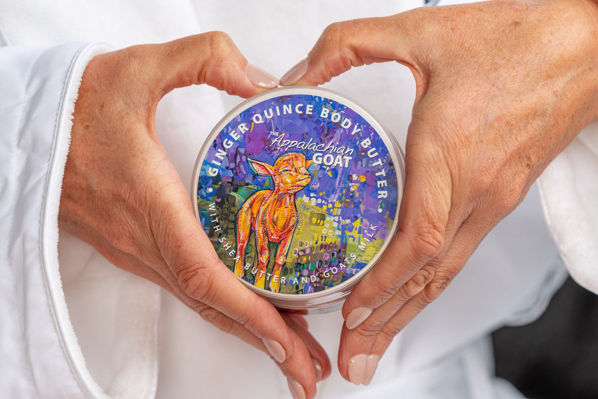 Goat milk body butter jar held between hands, round blue printed lid