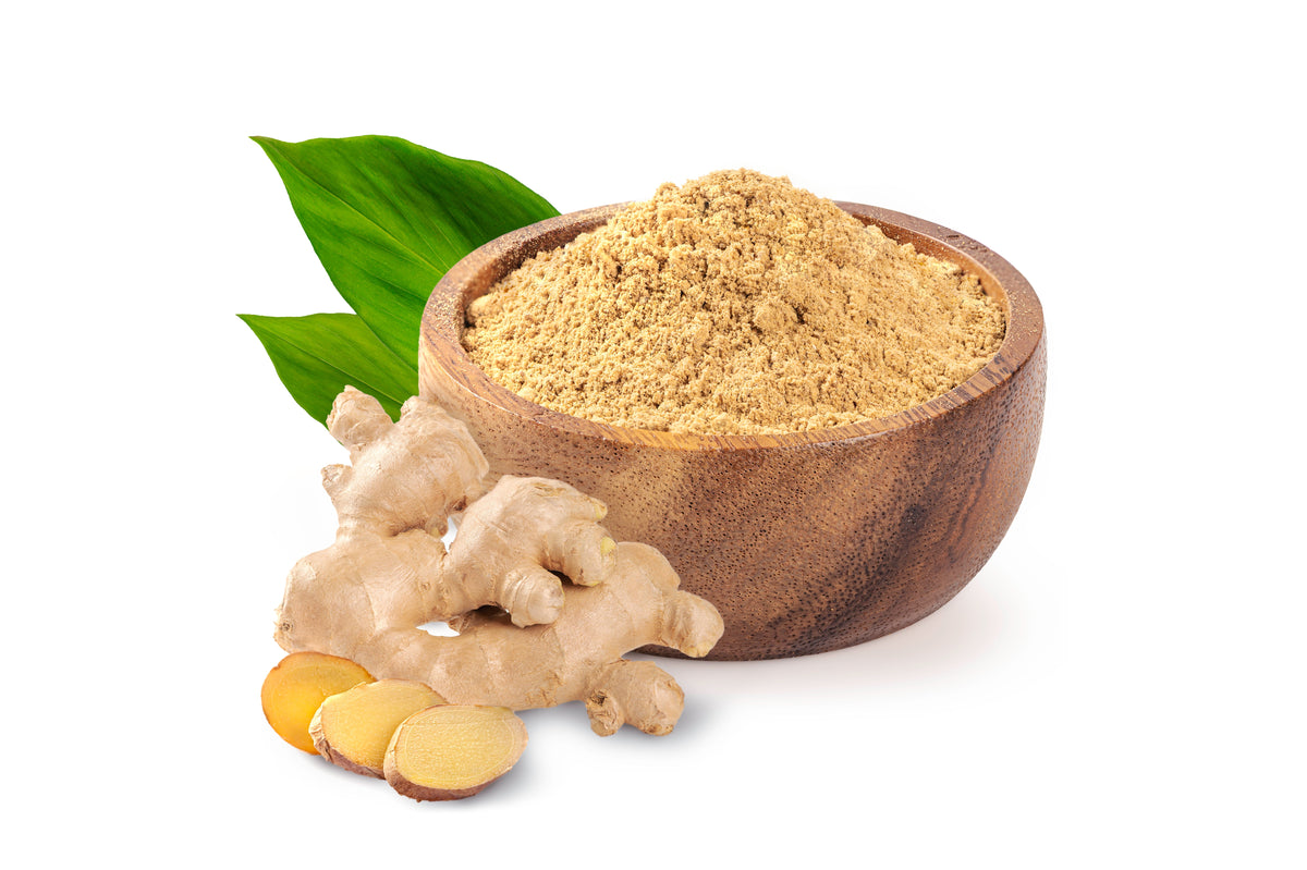 Wooden bowl of ginger root powder with fresh ginger pieces and green leaves
