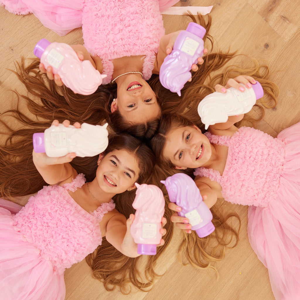 Kids holding unicorn-shaped shampoo and body wash bottles in pink and purple