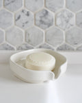 White glossy porcelain self-draining soap dish holding a cream soap bar