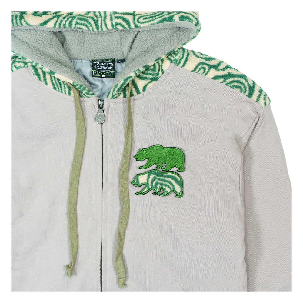Close-up of light gray zip-up hoodie with green drawcords, zipper, and bear emblem