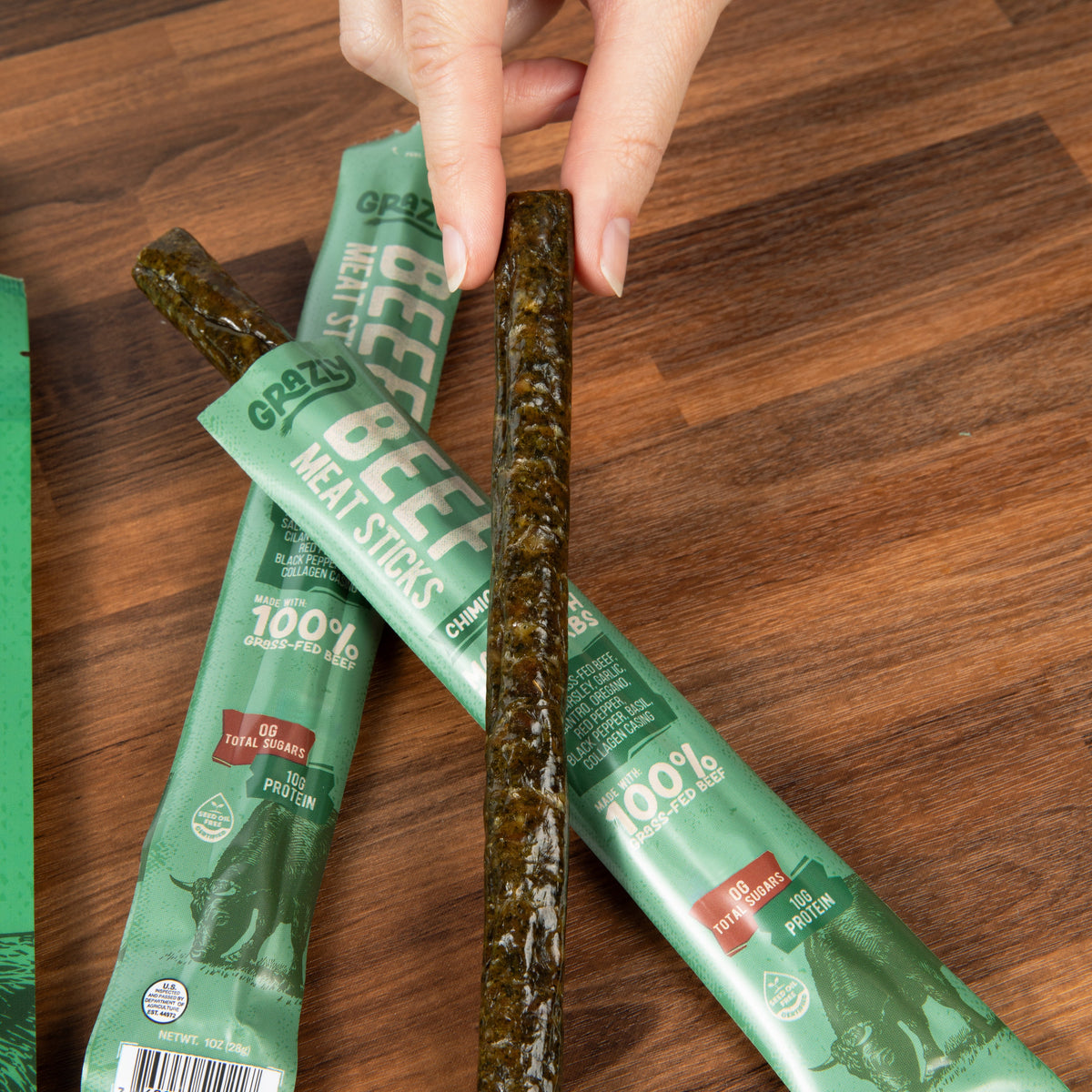 Chimichurri beef meat sticks pouches with a single stick on wooden surface