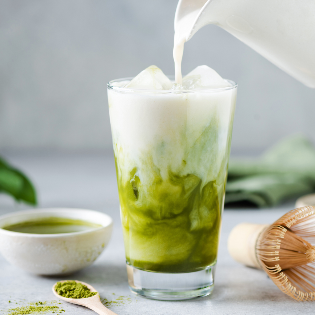 Clear glass of creamy green latte drink with milk pour, on ice