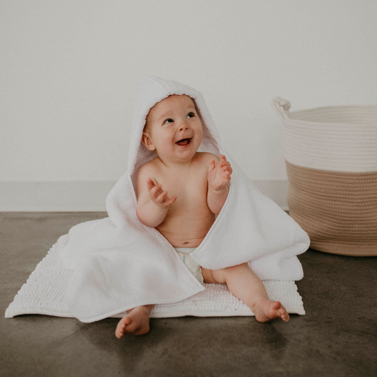 White hooded bath towel with baby lying down, hood up and towel draped