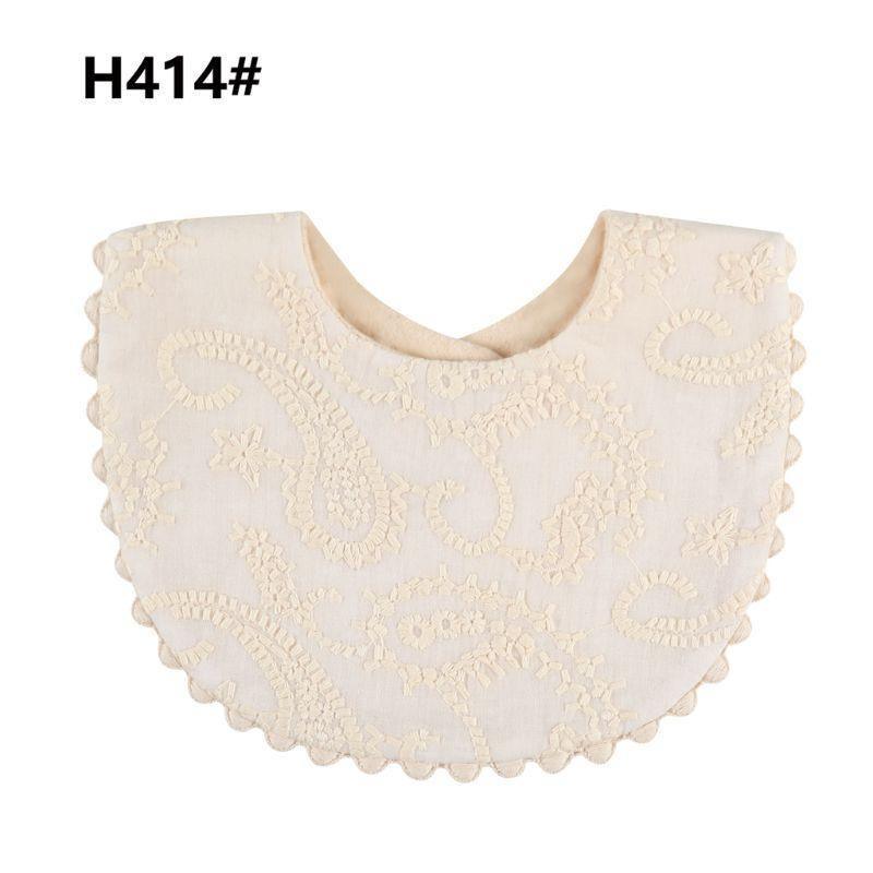Baby bib with pom-pom trim, cream fabric with raised embroidery swirl pattern