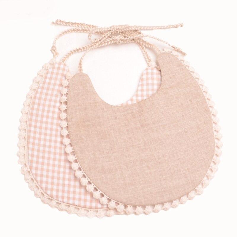 Beige linen-look and pink gingham double bib set with pom-pom trim and braided ties.