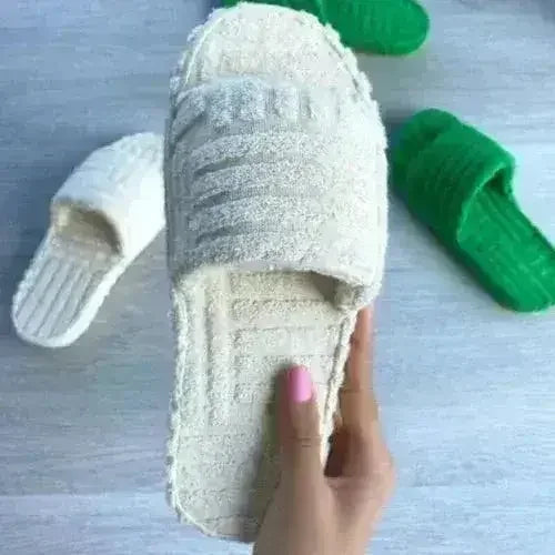 Light gray fuzzy open-toe slide slippers on feet with green socks.